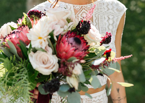 bride holding boho exotic bouquet dark garnet red and blush wedding florals