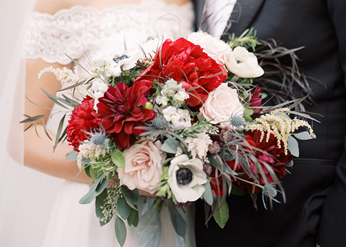 groom and bride holding bouquets red white blush wedding florals